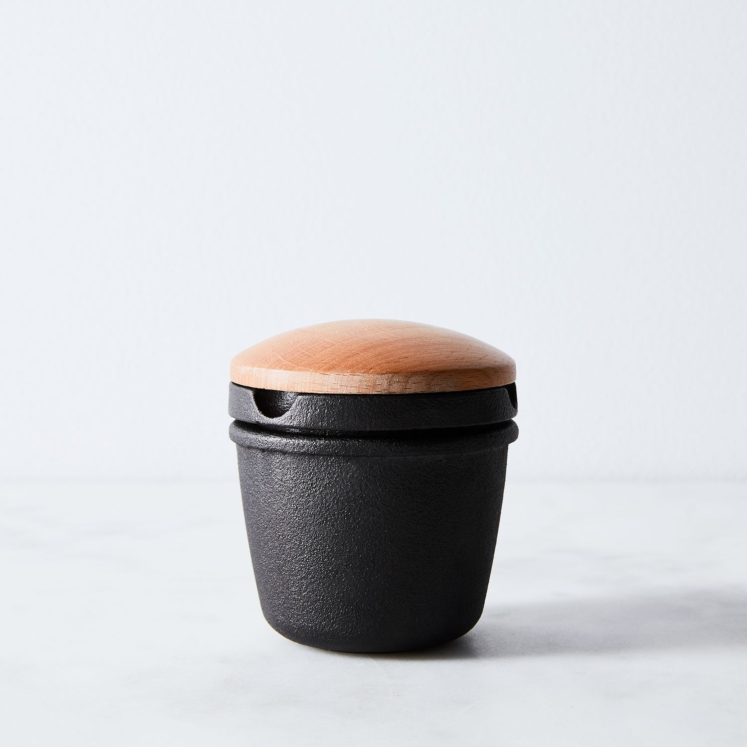 Black cast iron spice grinder with a wooden lid on a white surface.